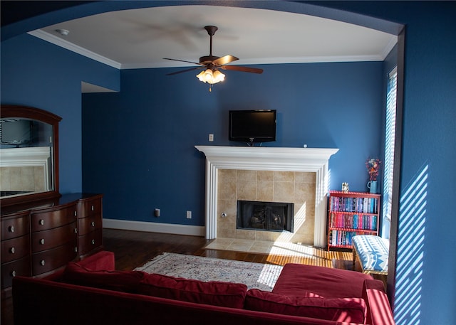 living area with wood finished floors, baseboards, a fireplace, ceiling fan, and crown molding