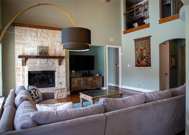 living room with wood finished floors, arched walkways, a stone fireplace, baseboards, and a towering ceiling