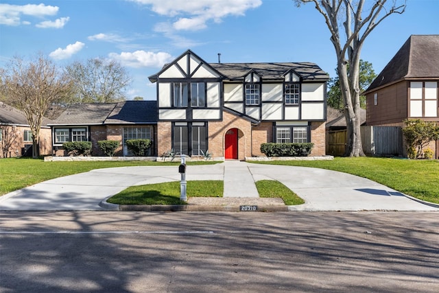 tudor house featuring fence, driveway, stucco siding, a front lawn, and brick siding