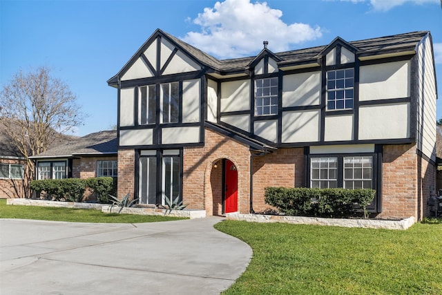 tudor home with a front yard, brick siding, driveway, and stucco siding