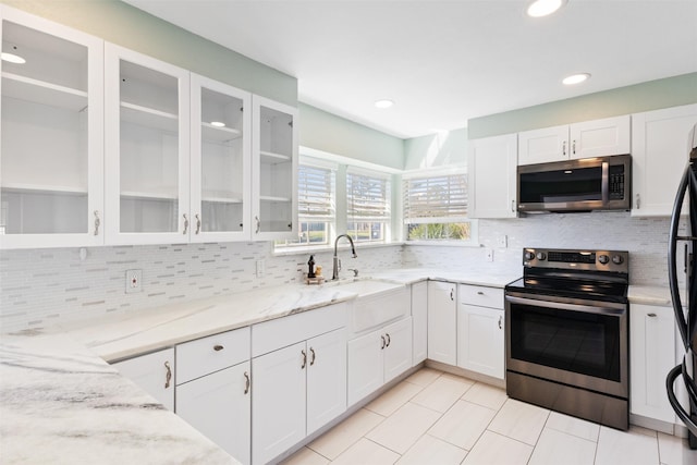 kitchen featuring backsplash, light stone counters, stainless steel appliances, white cabinetry, and a sink