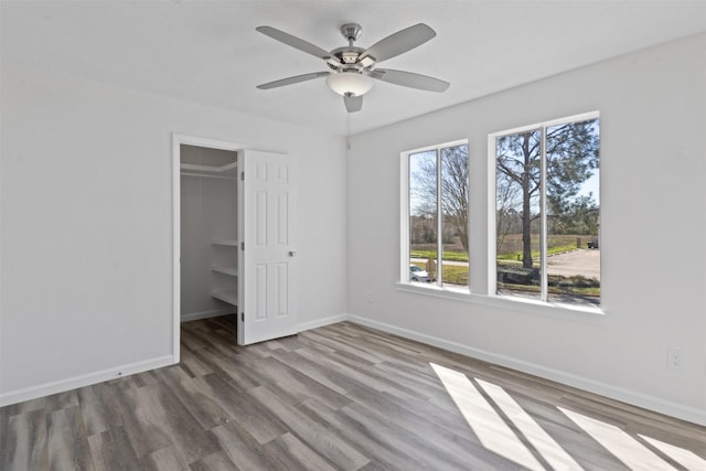 unfurnished bedroom featuring a closet, a walk in closet, baseboards, and wood finished floors