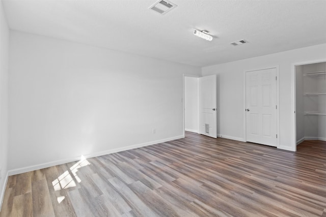 unfurnished bedroom featuring a textured ceiling, wood finished floors, visible vents, and baseboards