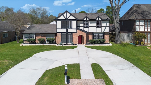 english style home with a front lawn, brick siding, driveway, and stucco siding