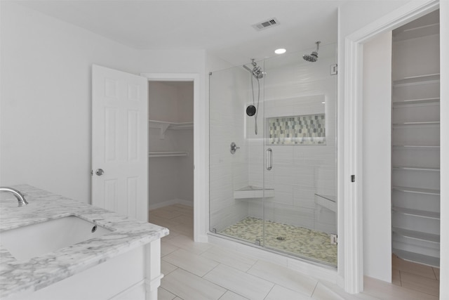 bathroom featuring vanity, visible vents, tile patterned flooring, a shower stall, and a walk in closet