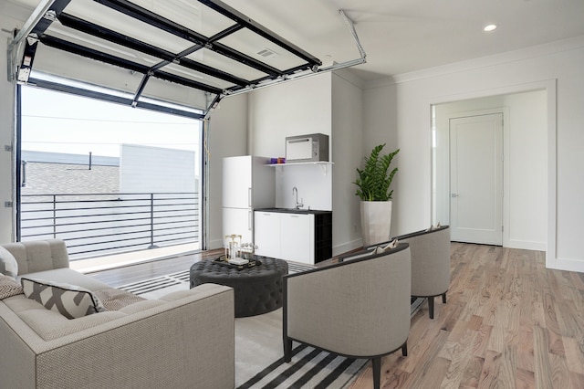 living area featuring recessed lighting, baseboards, light wood finished floors, a garage, and wet bar