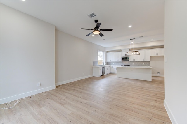 unfurnished living room with visible vents, light wood-style flooring, a ceiling fan, and baseboards