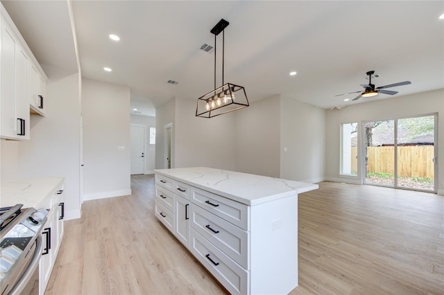 kitchen featuring light wood finished floors, recessed lighting, white cabinets, gas range oven, and a center island