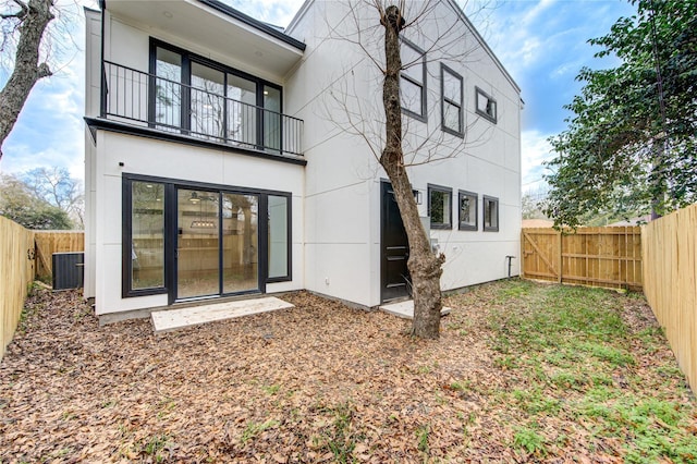 rear view of property with a fenced backyard, central air condition unit, stucco siding, and a balcony