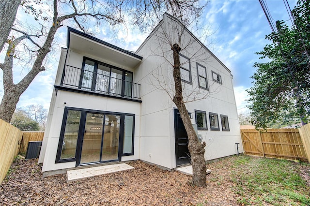 back of house with stucco siding, a balcony, and a fenced backyard