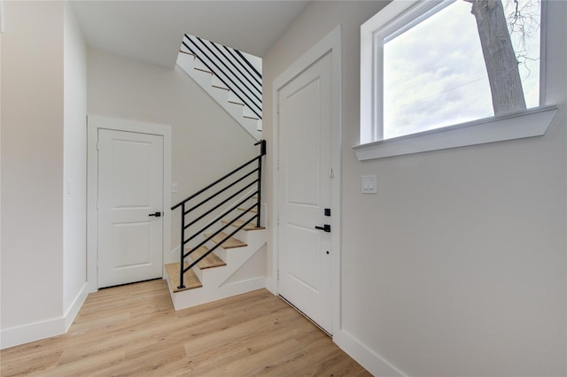 foyer entrance with stairs, light wood-style floors, and baseboards