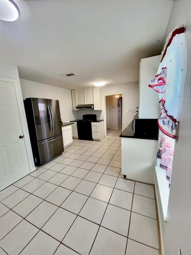 kitchen with black gas range, dark countertops, freestanding refrigerator, white cabinets, and light tile patterned floors