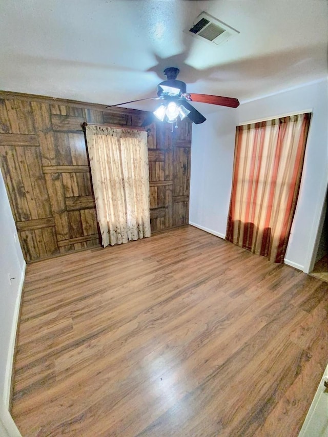 unfurnished room featuring visible vents, ceiling fan, wooden walls, and wood finished floors