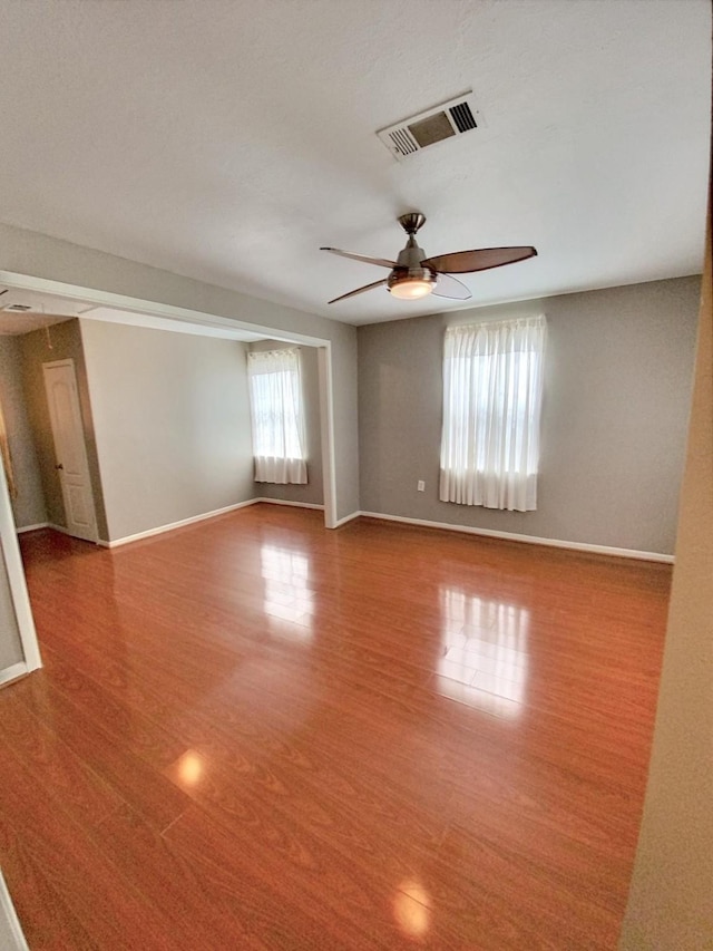 empty room with a ceiling fan, wood finished floors, visible vents, and baseboards