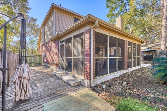 view of side of home with a wooden deck, fence, a sunroom, and a chimney