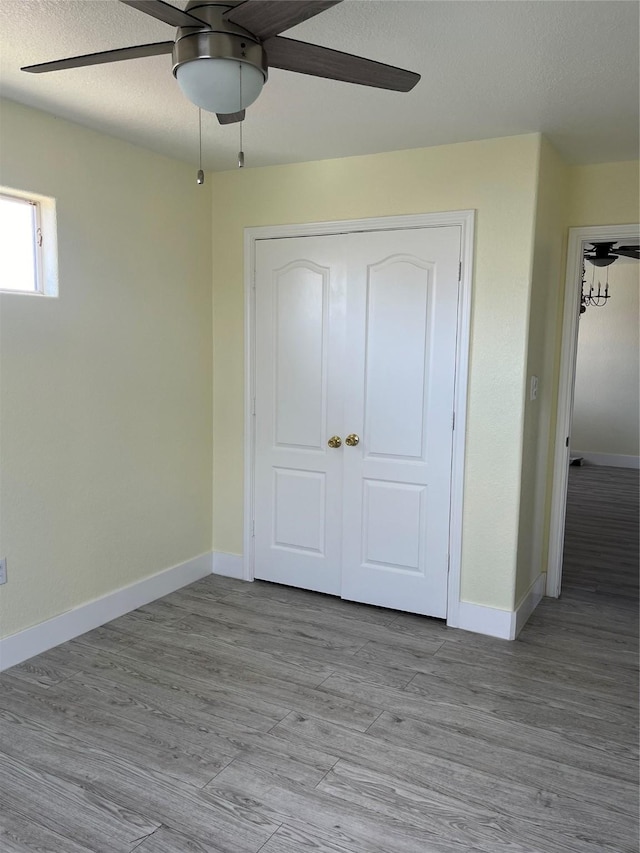 unfurnished bedroom featuring ceiling fan, a textured ceiling, baseboards, and light wood-style floors