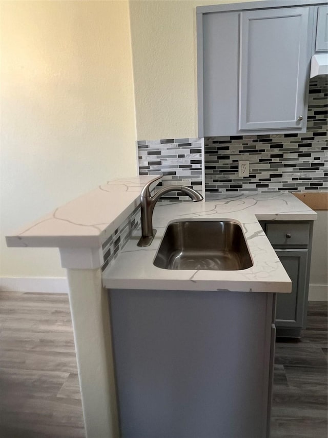 kitchen featuring backsplash, gray cabinetry, light stone countertops, and a sink