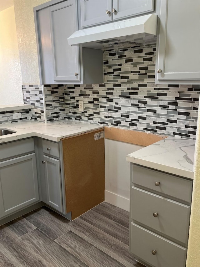 kitchen featuring under cabinet range hood, decorative backsplash, light stone counters, and gray cabinets