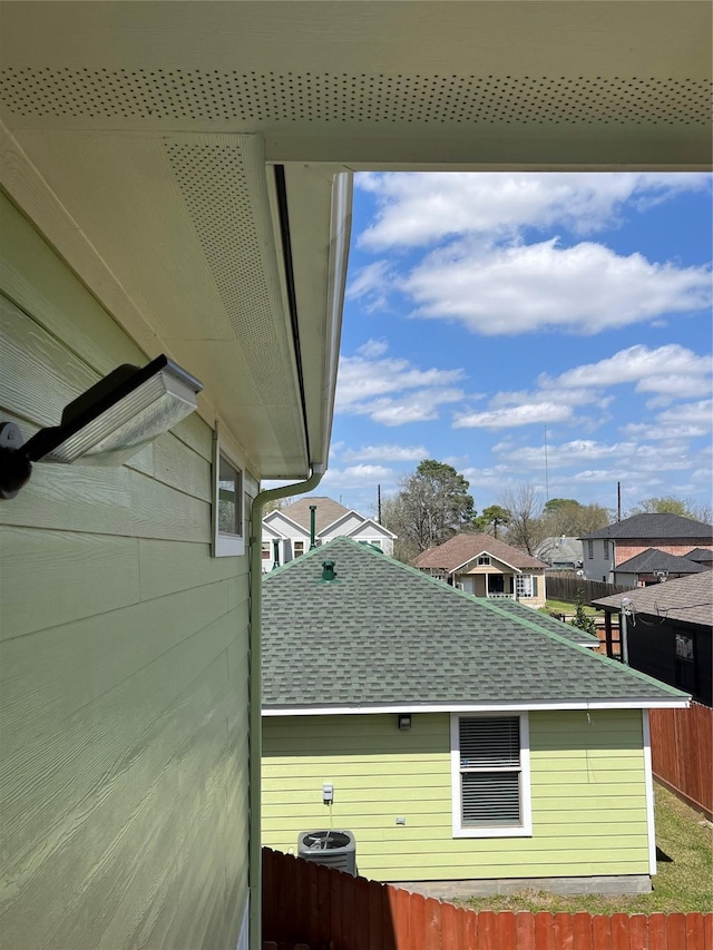 view of side of home with a shingled roof, central AC, and fence