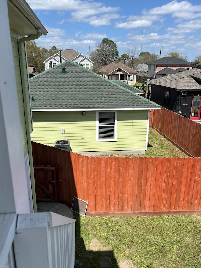 view of property exterior with a yard, roof with shingles, central AC, and fence