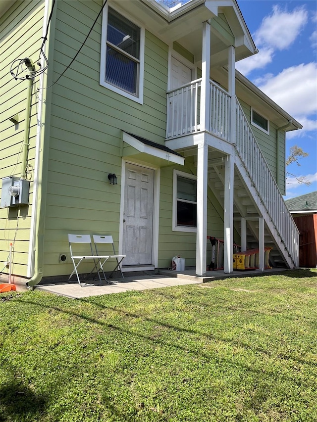 rear view of property with stairs, a patio, and a lawn