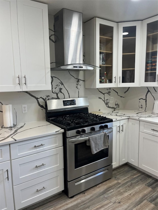 kitchen with dark wood-type flooring, stainless steel gas range, decorative backsplash, white cabinetry, and wall chimney exhaust hood