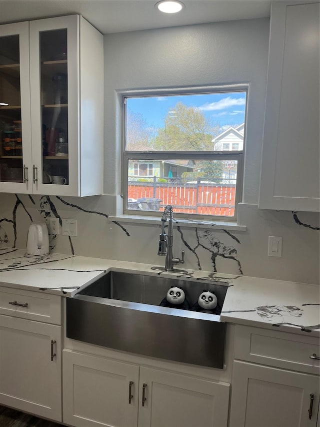 kitchen with backsplash, glass insert cabinets, light countertops, white cabinets, and a sink