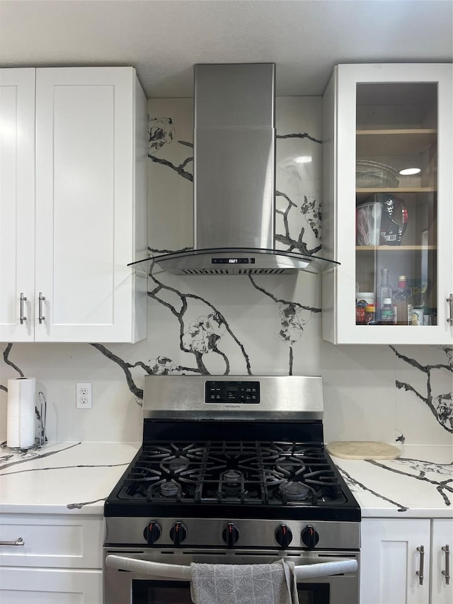 kitchen with light countertops, white cabinets, wall chimney exhaust hood, and gas stove