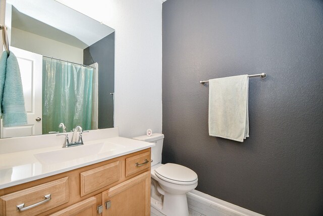 bathroom with toilet, a shower with shower curtain, baseboards, vanity, and a textured wall