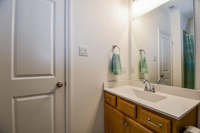 full bathroom with visible vents, vanity, and a textured wall