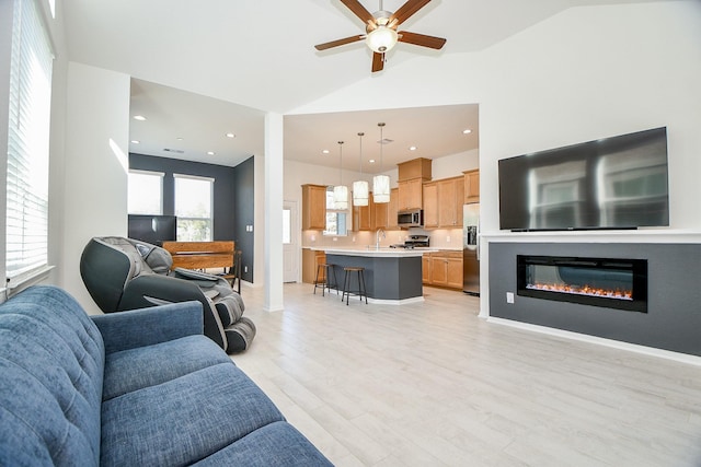 living room with a ceiling fan, lofted ceiling, recessed lighting, light wood-style floors, and a glass covered fireplace