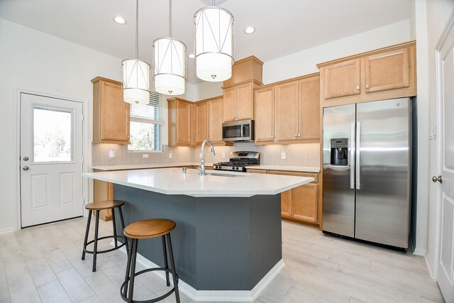 kitchen featuring a kitchen bar, an island with sink, tasteful backsplash, stainless steel appliances, and light countertops