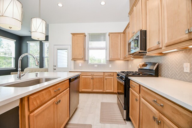 kitchen featuring tasteful backsplash, decorative light fixtures, light countertops, appliances with stainless steel finishes, and a sink