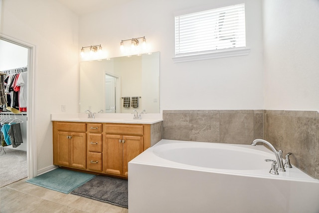 bathroom with double vanity, a walk in closet, a garden tub, and a sink