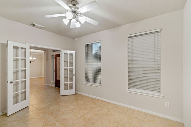 tiled spare room with visible vents, ceiling fan with notable chandelier, french doors, and baseboards