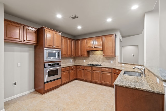 kitchen featuring light stone counters, a peninsula, a sink, decorative backsplash, and stainless steel appliances