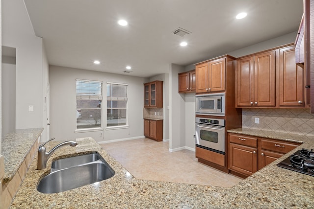 kitchen with a sink, light stone counters, brown cabinets, and appliances with stainless steel finishes