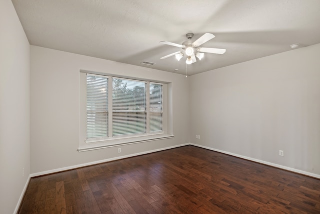 empty room with ceiling fan, visible vents, baseboards, and dark wood-style floors