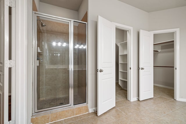 full bathroom featuring tile patterned flooring, a walk in closet, baseboards, and a stall shower