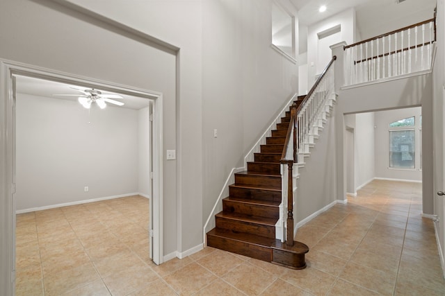 staircase featuring tile patterned floors, baseboards, a towering ceiling, and a ceiling fan