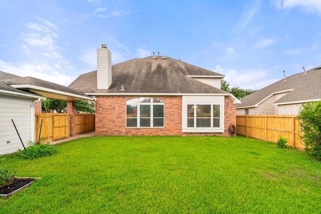 rear view of house featuring brick siding, roof with shingles, a lawn, a chimney, and a fenced backyard