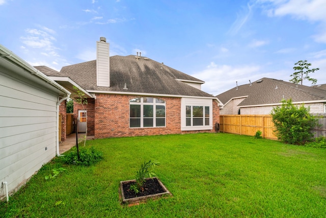 rear view of property featuring roof with shingles, a chimney, fence private yard, a lawn, and brick siding