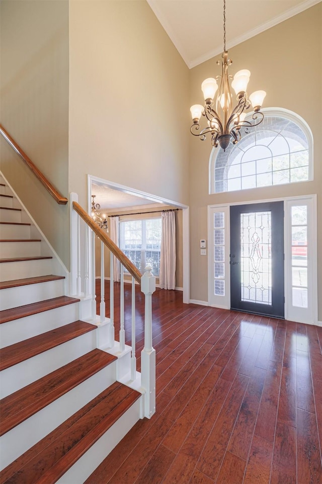 foyer with stairway, ornamental molding, a towering ceiling, an inviting chandelier, and dark wood-style flooring