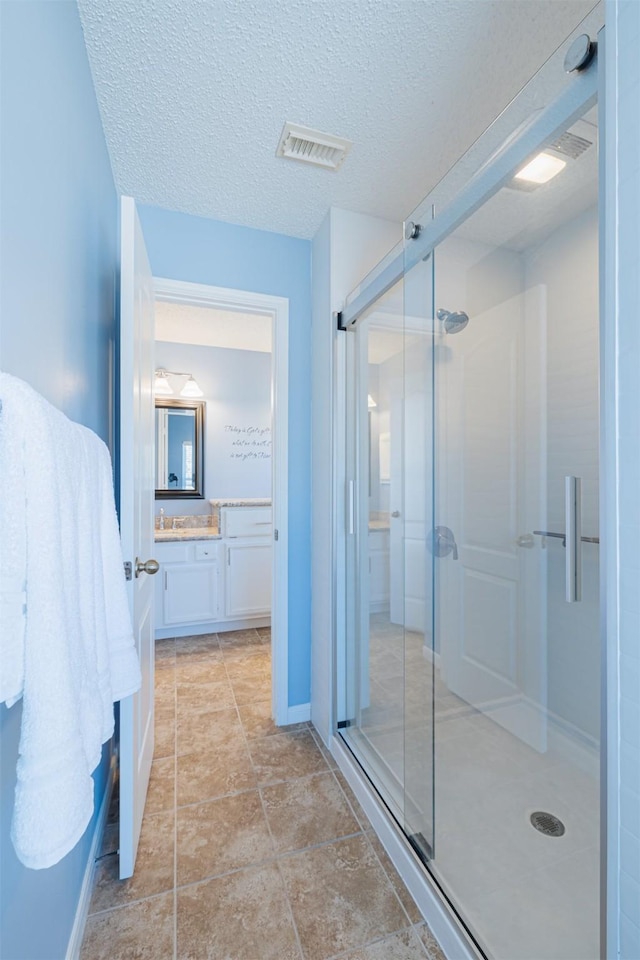 full bath with a textured ceiling, vanity, visible vents, and a stall shower