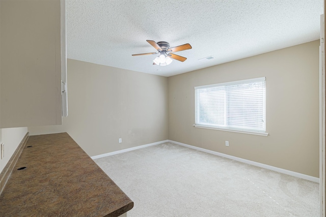 unfurnished room featuring visible vents, a ceiling fan, a textured ceiling, baseboards, and light colored carpet