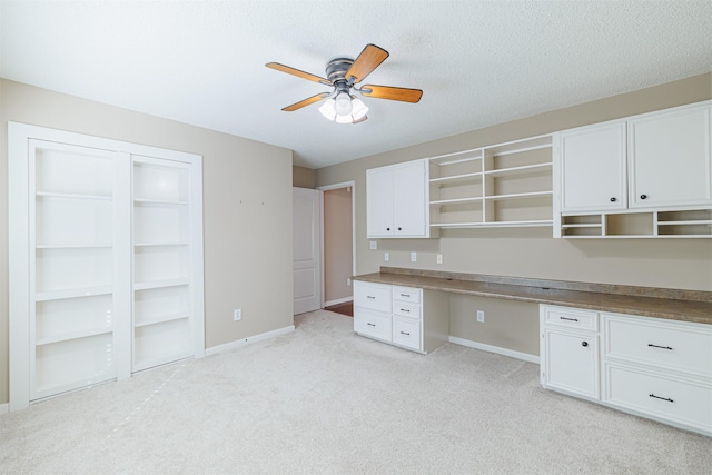 unfurnished office featuring light carpet, built in desk, baseboards, and ceiling fan