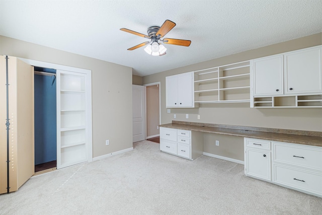 office area with baseboards, ceiling fan, light colored carpet, built in desk, and a textured ceiling