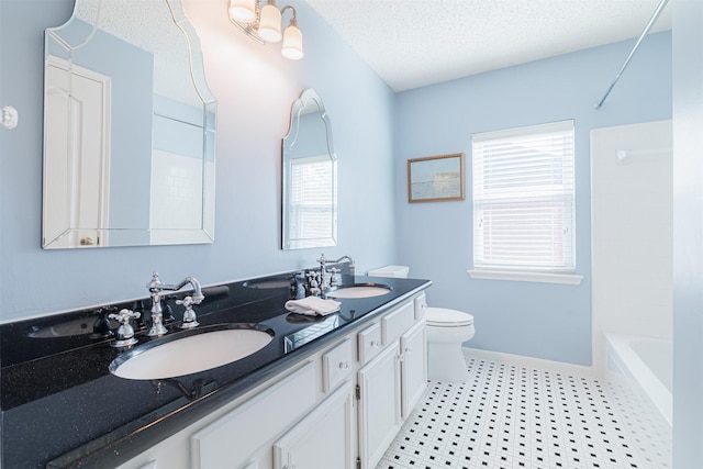 full bathroom with toilet, a textured ceiling, baseboards, and a sink