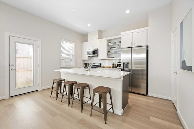 kitchen featuring a center island with sink, a breakfast bar area, decorative backsplash, appliances with stainless steel finishes, and open shelves