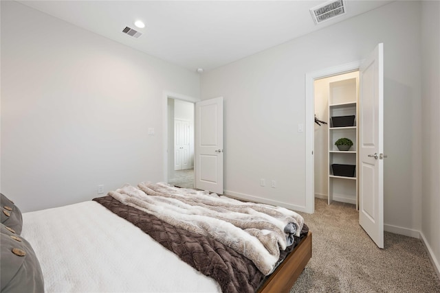 bedroom featuring a spacious closet, light colored carpet, visible vents, and baseboards